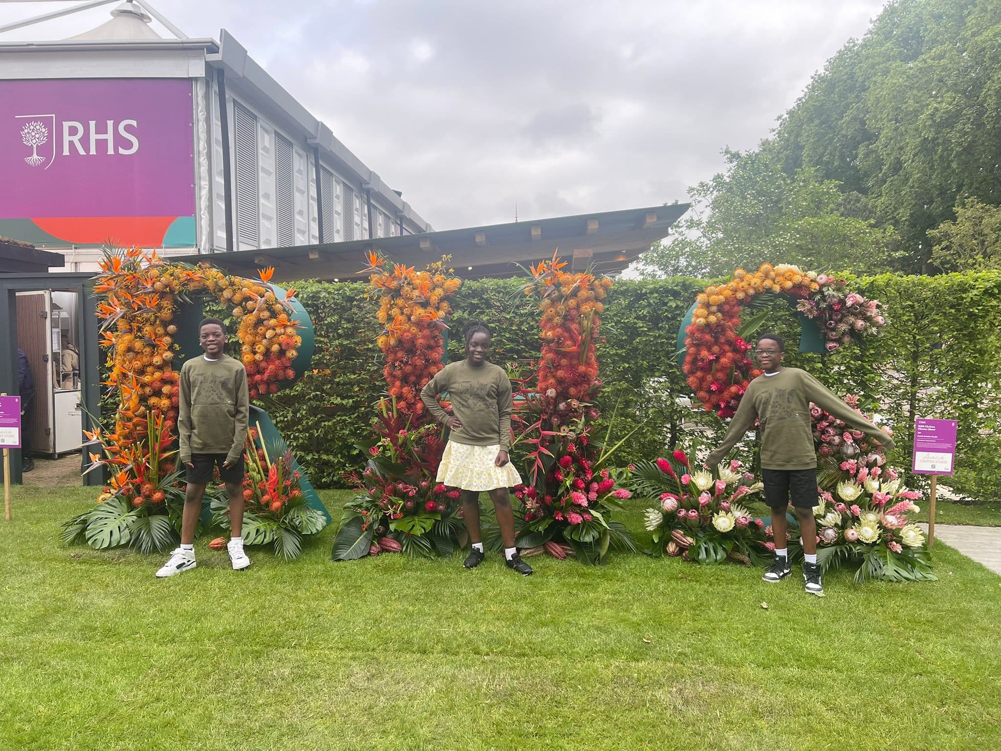 Planet Trio at the RHS Chelsea Flower Show standing before floral RHS letters